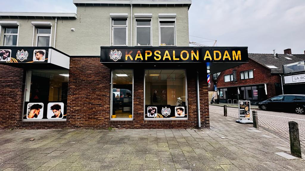De gevel van Kapsalon Adam aan de Hoofdstraat 25, met het zwarte bord en de gouden letters